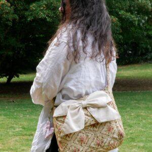 femme qui porte un sac bandoulière tissé fleuri et rose, vert avec un gros nœud